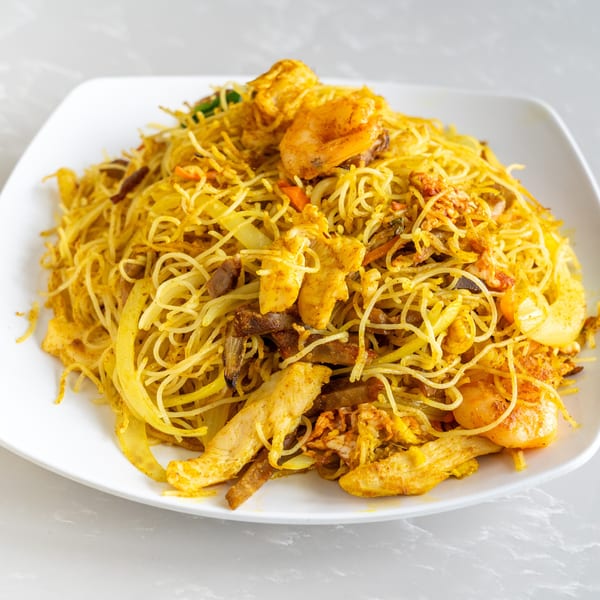Close-up of Singapore-style vermicelli noodles with chicken, shrimp, and vegetables on a white plate.