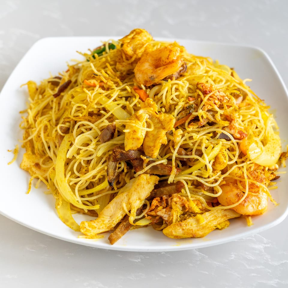 Close-up of Singapore-style vermicelli noodles with chicken, shrimp, and vegetables on a white plate.