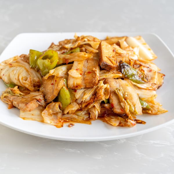 Stir-fried pork belly with cabbage and green peppers on a white plate.