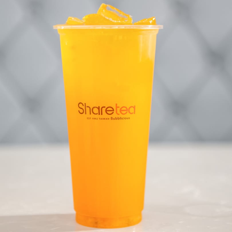 Sharetea mango drink with ice in a clear plastic cup on a white surface.