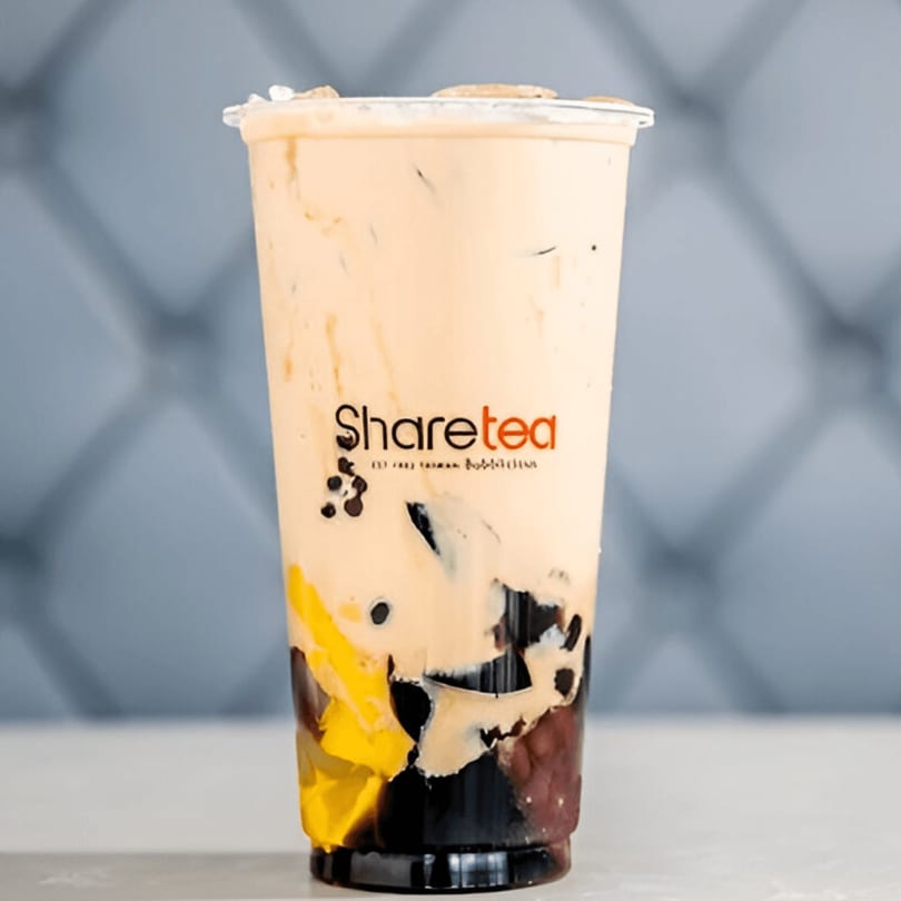 Sharetea boba drink with light brown liquid, dark boba, and yellow fruit pieces in a clear cup.