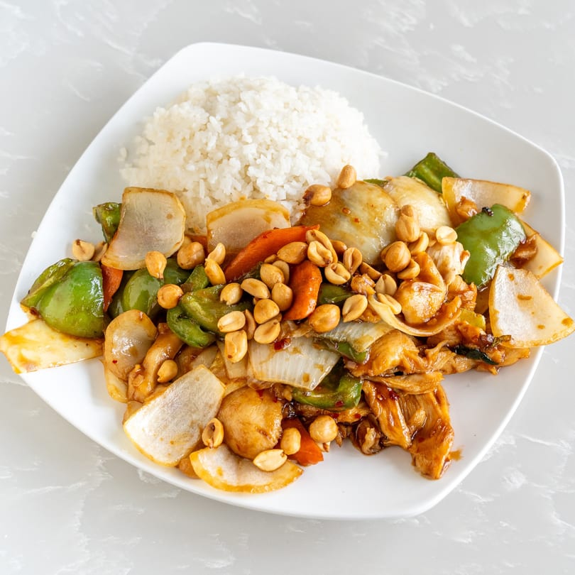 Kung Pao Chicken with white rice, peanuts, green peppers, and onions on a white plate.