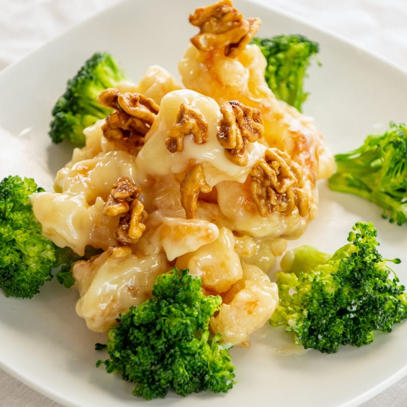 Honey walnut shrimp with creamy sauce and broccoli florets on a white plate.